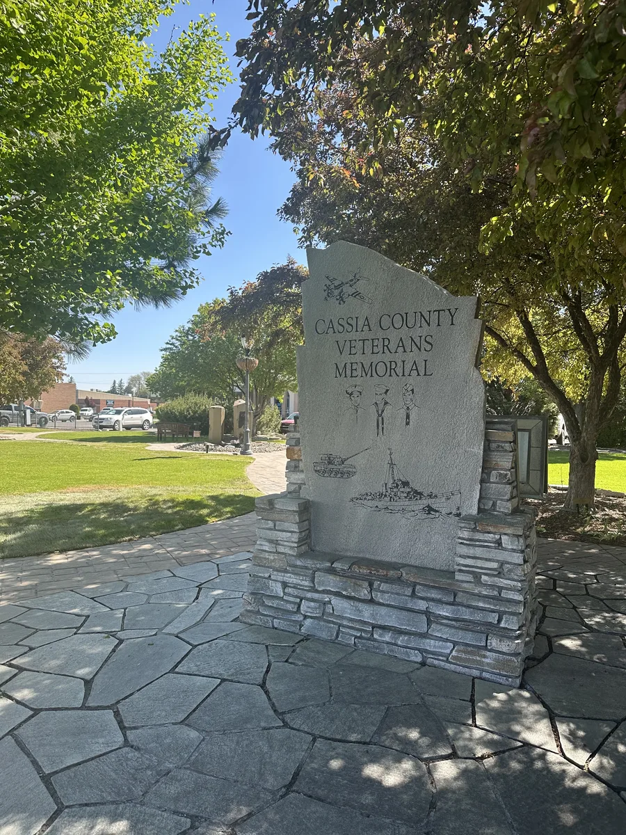 The Cassia County Veterans Memorial in Burley: an engraved stone monument on a flagstone plaza under shade trees.
